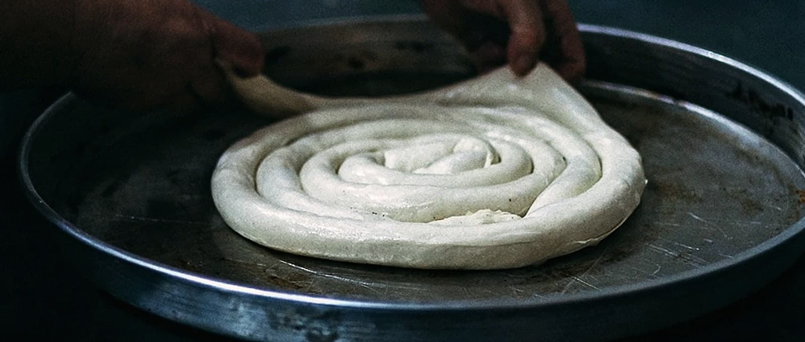 Hands laying coiled pastry into a round tepsija